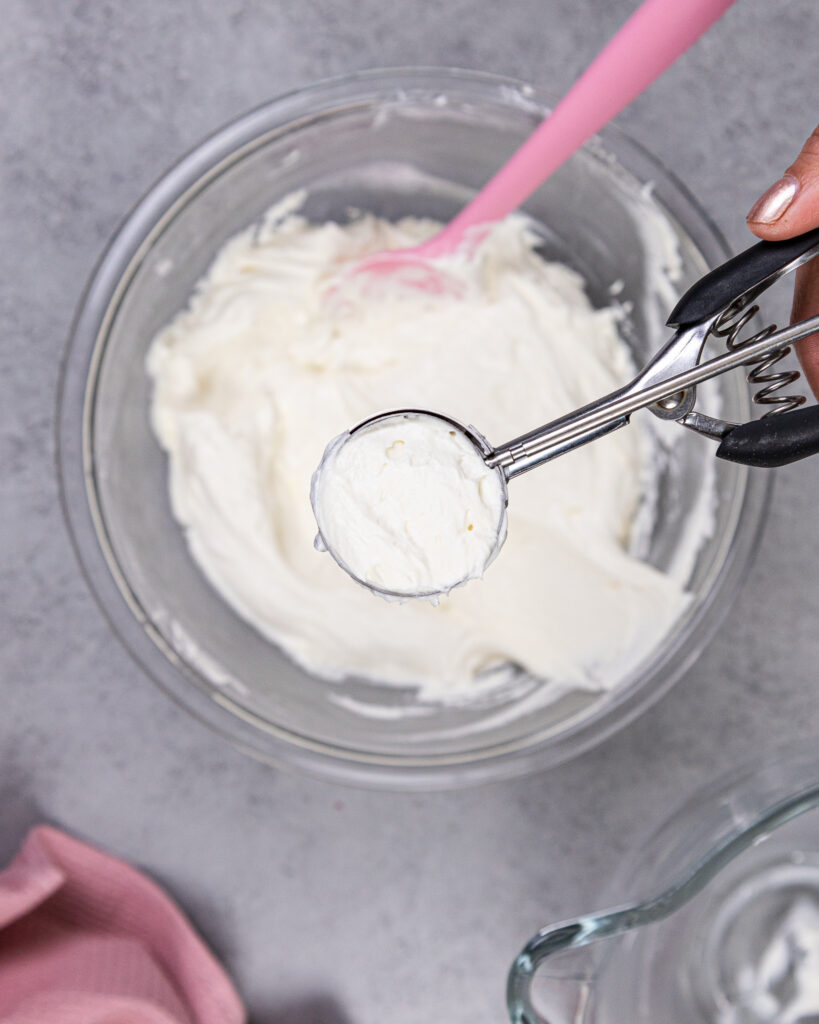 image of a no bake cheesecake filling being scooped using a cookie scoop to make no bake cheesecake bites