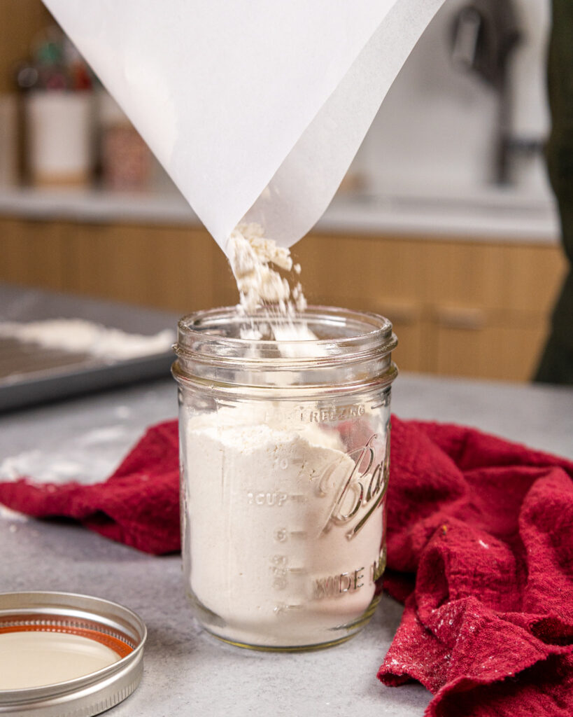 image of heat treated flour being poured into a mason jar for storage for future use