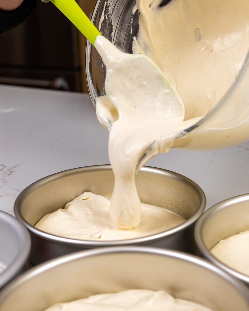 image of fluffy white cake batter being poured into an 8-inch pan