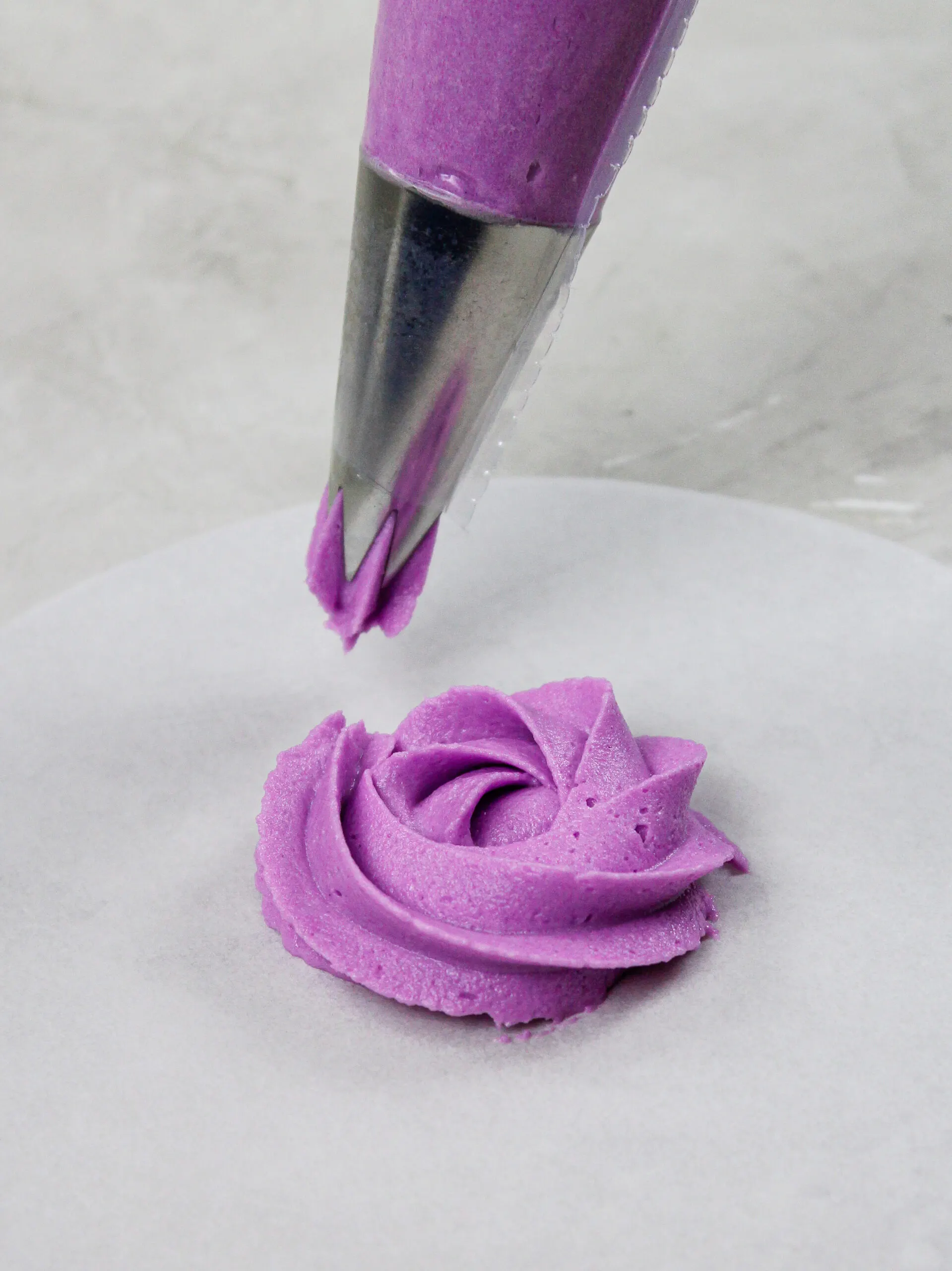 image of a buttercream rosette being piped on a piece of parchment paper to practice the motion with a wilton 1m frosting tip