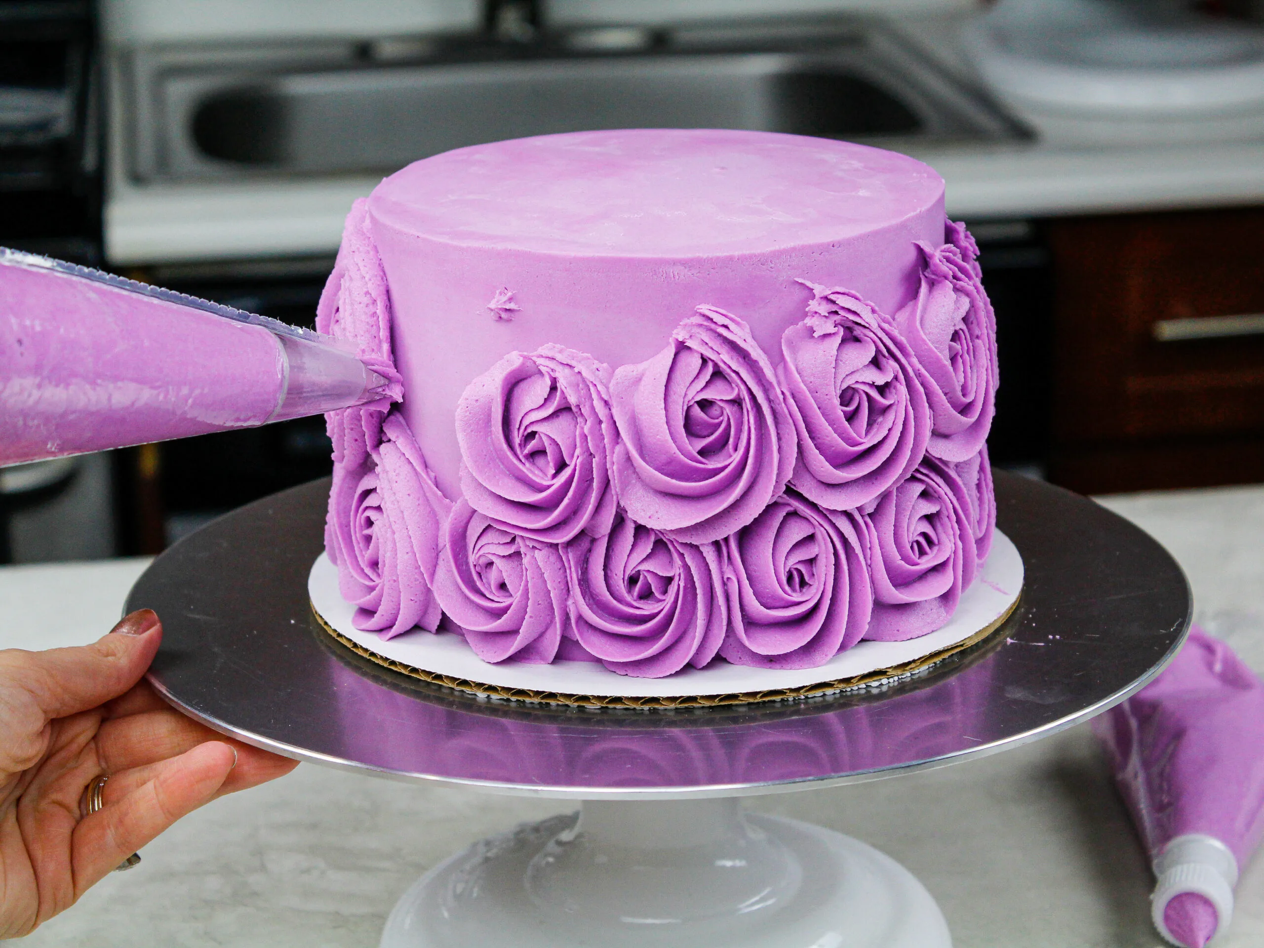image a of a purple buttercream rosettes being piped around a cake with a wilton 1m frosting tip