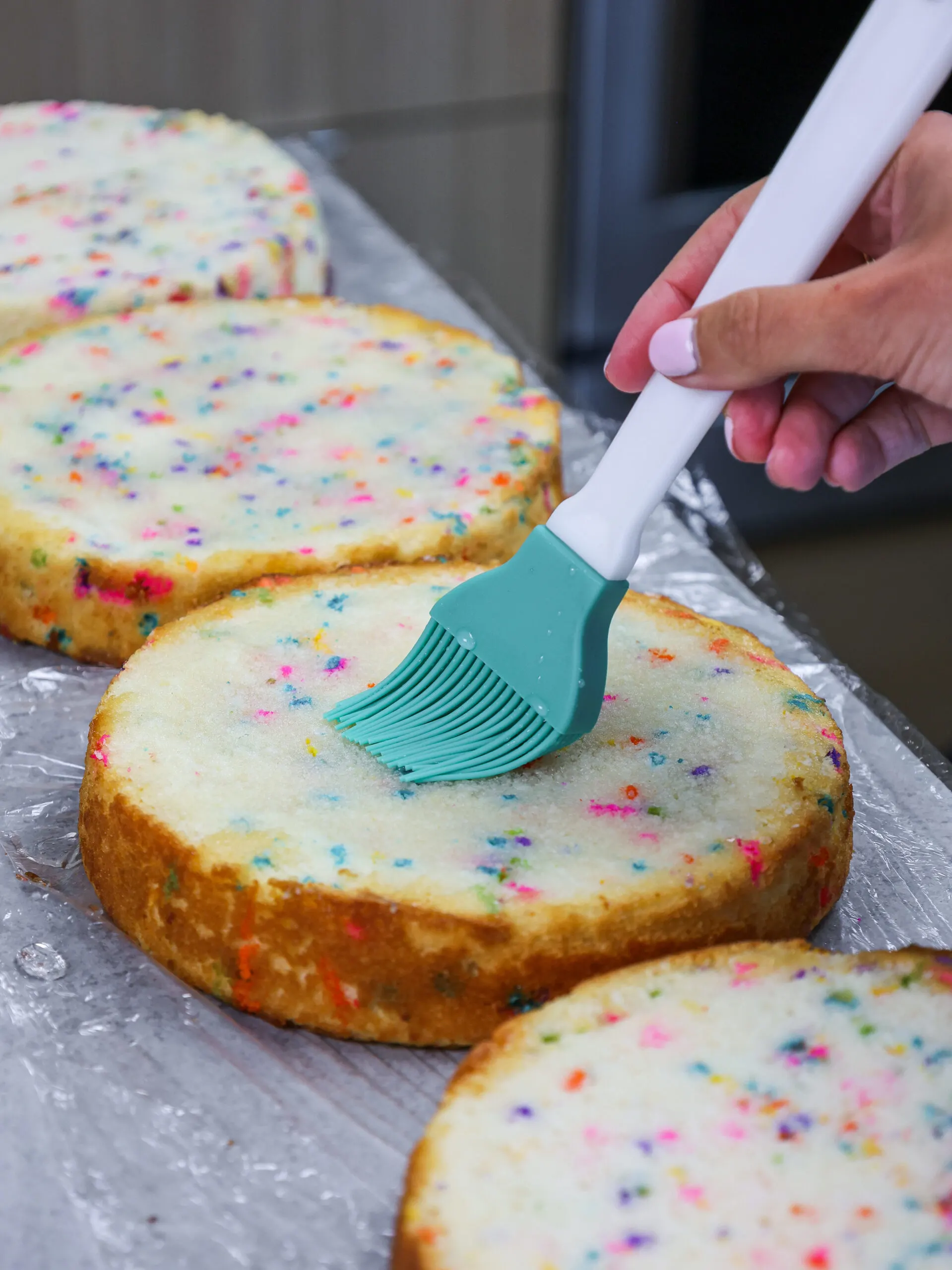 image of simple syrup being brushed onto a funfetti cake layer