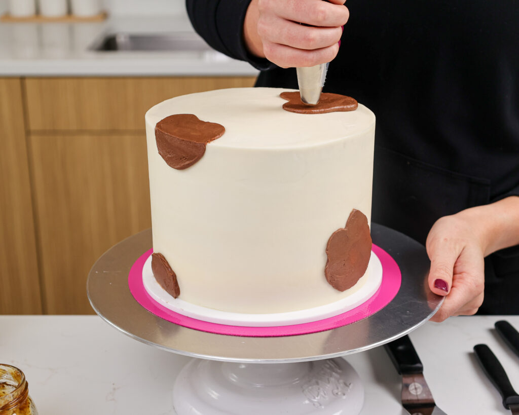image of a cake being frosted with chocolate frosting spots to make a goat cake