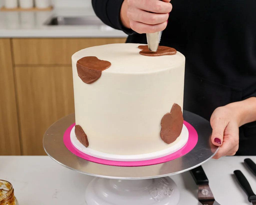 image of a cake being frosted with chocolate frosting spots to make a goat cake