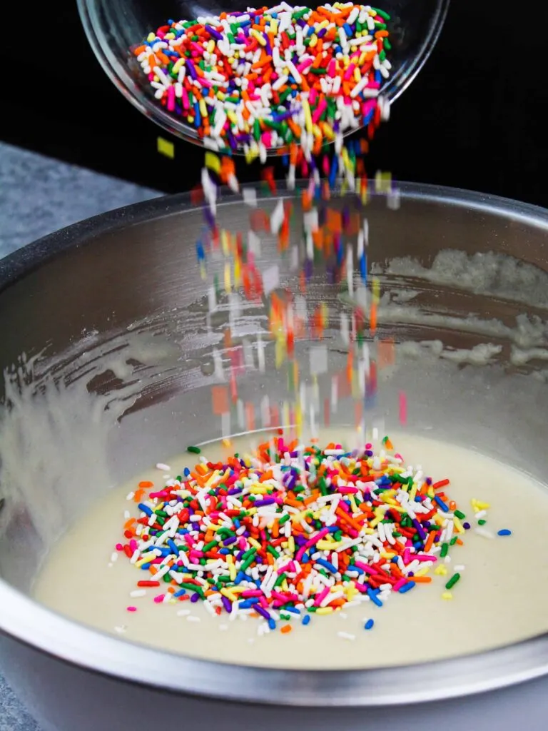 image of vegan sprinkles being poured into a vegan vanilla cake also known as a wacky cake