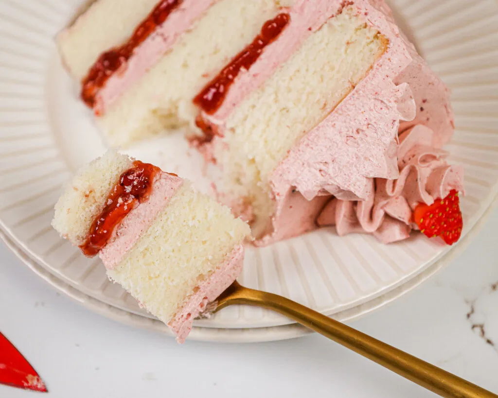 image of a slice of a vanilla and strawberry cake on a plate that's been cut into with a fork