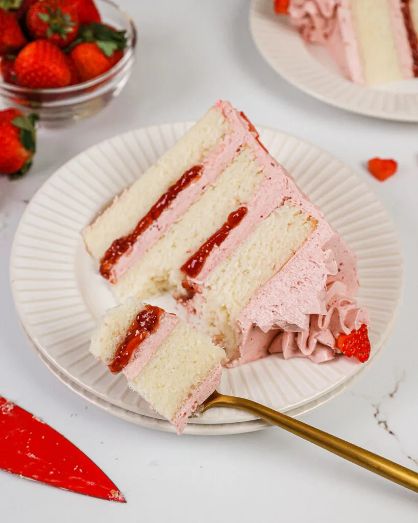 image of a slice of a vanilla and strawberry cake on a plate that's been cut into with a fork shared as part of a berry recipe round up