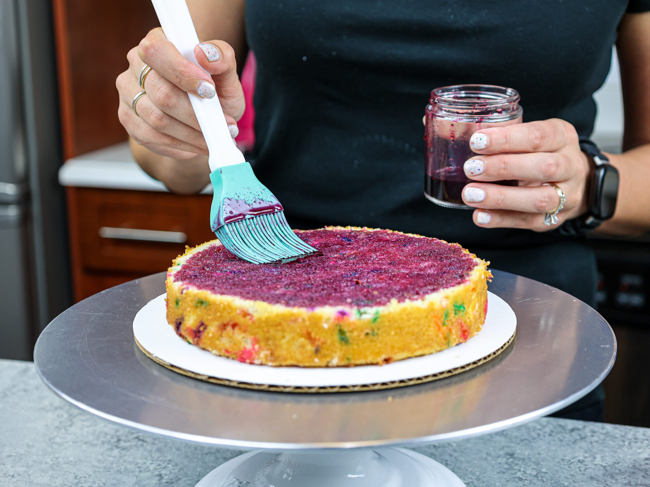image of blueberry simple syrup being brushed onto a cake layer