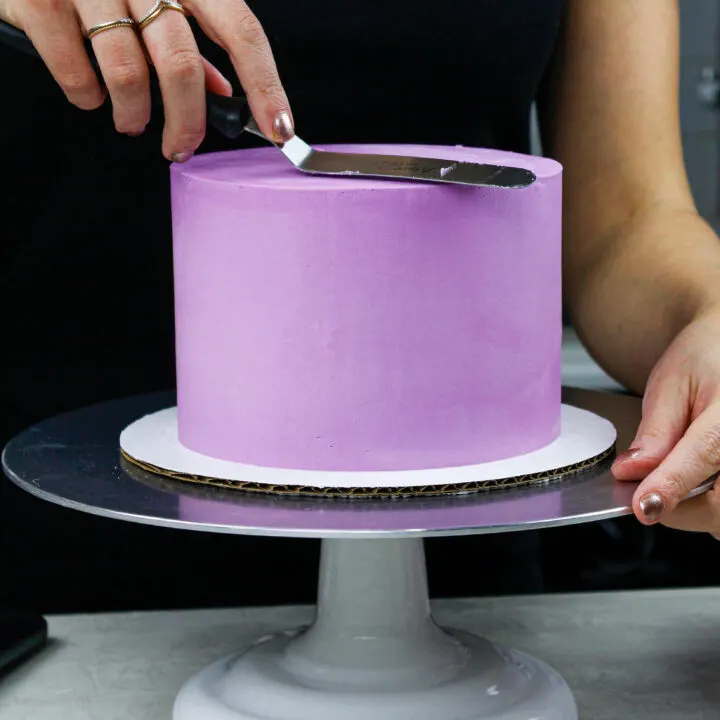 image of a buttercream cake being frosted with sharp edges and smooth sides to show How to Frost a Cake Smoothly