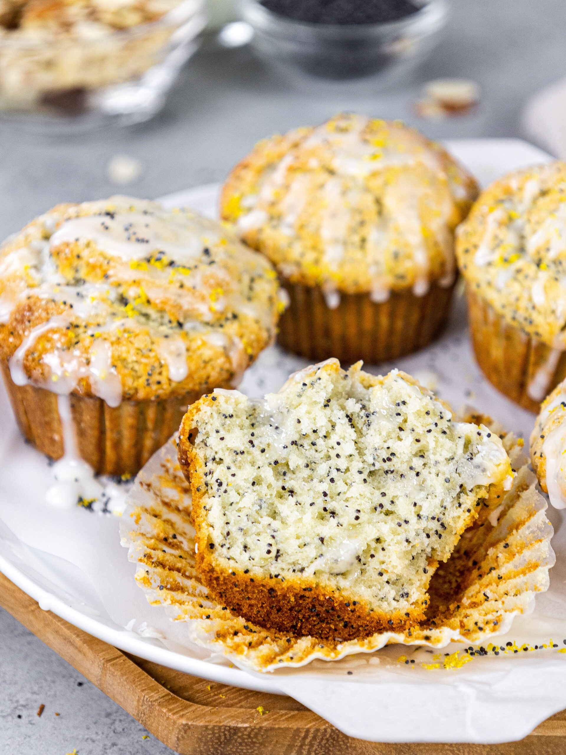 image of almond poppy seed muffins glazed with almond glaze sitting on a tray with one cut open to show how fluffy and tender the inside is