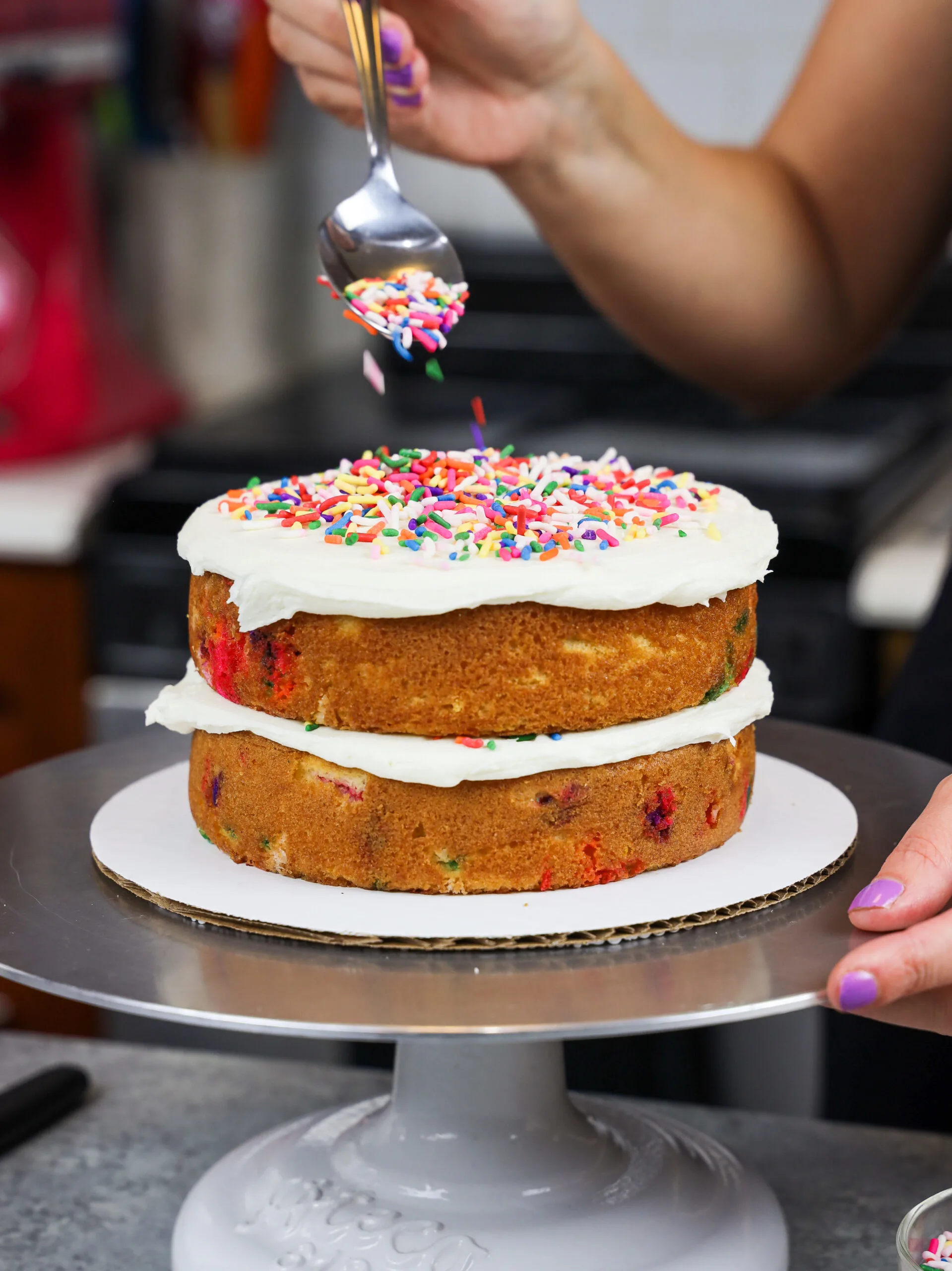 image of rainbow sprinkles being added between the cake layers of a gluten free funfetti cake 