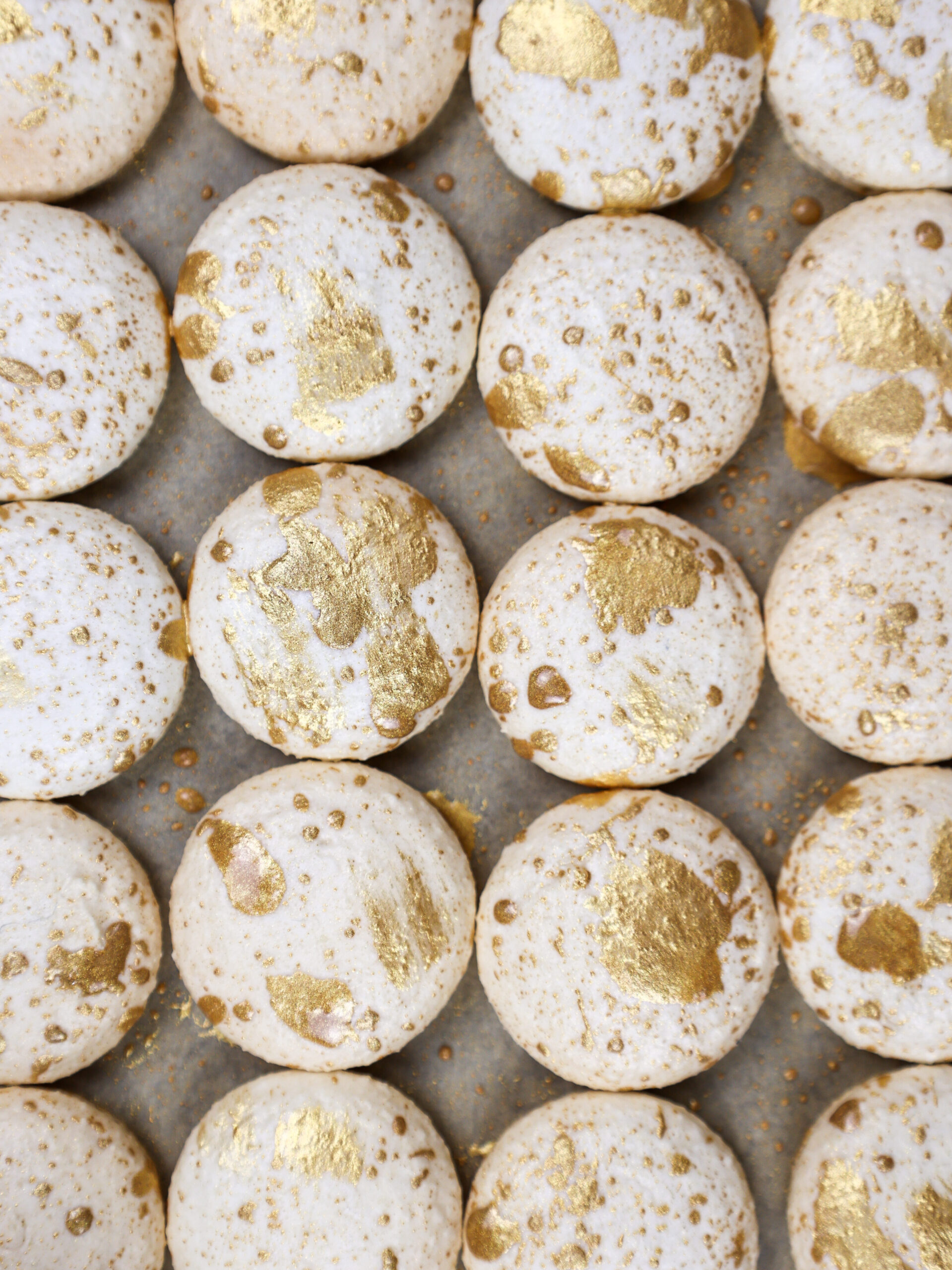 image of white vanilla macaron shells that have been splattered and brushed with edible gold paint