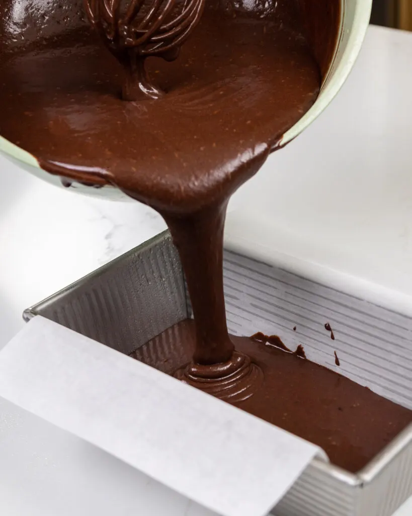 image of chocolate cake batter being poured into a loaf pan.