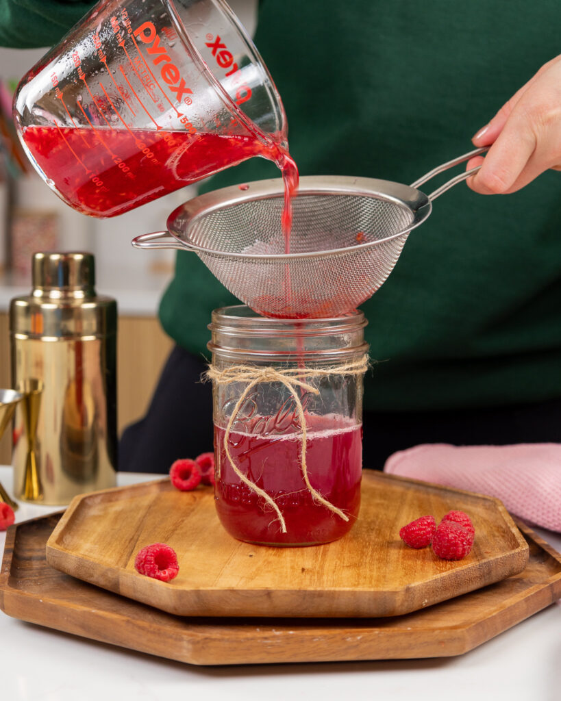 image of raspberry simple syrup being poured through a strainer
