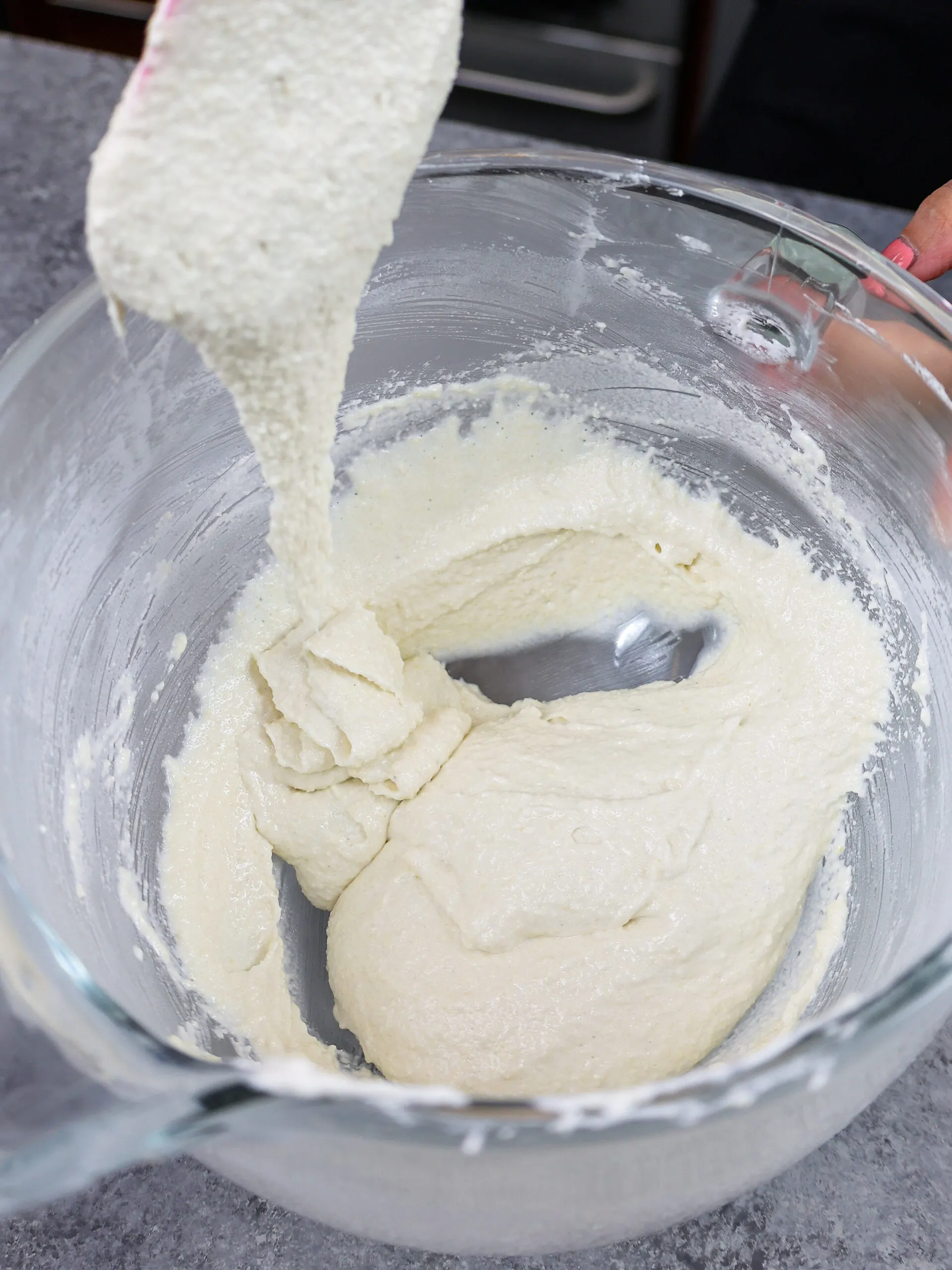image of white vanilla macaron batter flowing off a rubber spatula in thick ribbons indicating it has been mixed perfectly and is ready to be piped