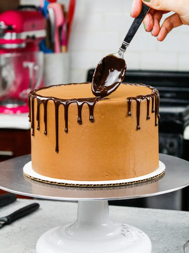 image of chocolate ganache drips being added to a chocolate drip cake with a spoon
