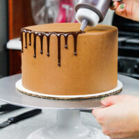 image of chocolate ganache drips being added to a chocolate drip cake using a plastic bottle