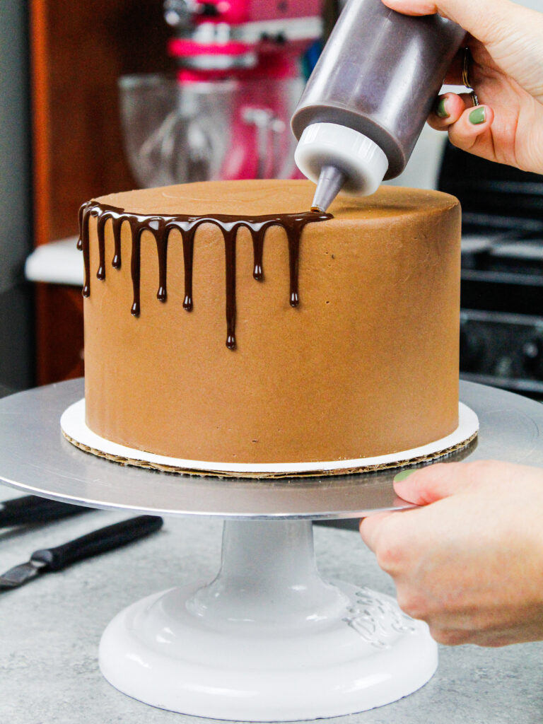 image of chocolate ganache drips being added to a chocolate drip cake using a plastic bottle