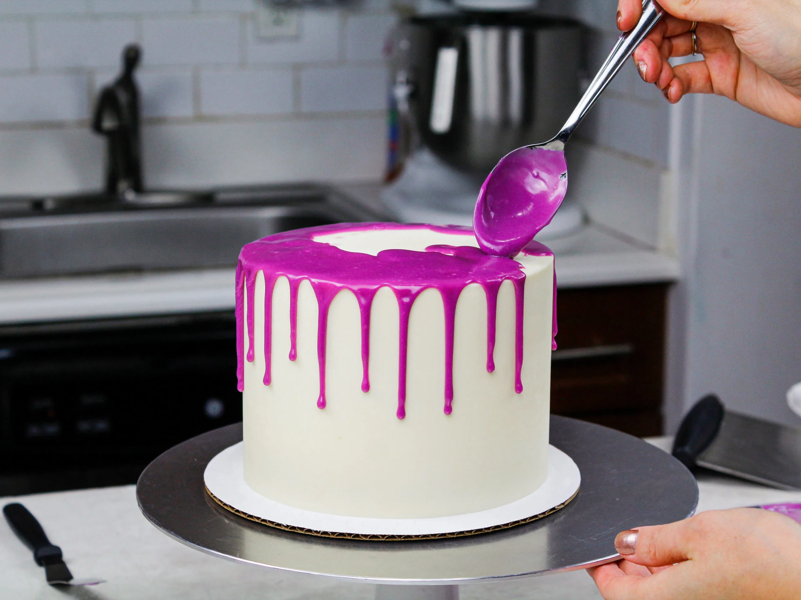 image of white choc ganache drips being added to a chilled buttercream cake to make a purple drip cake