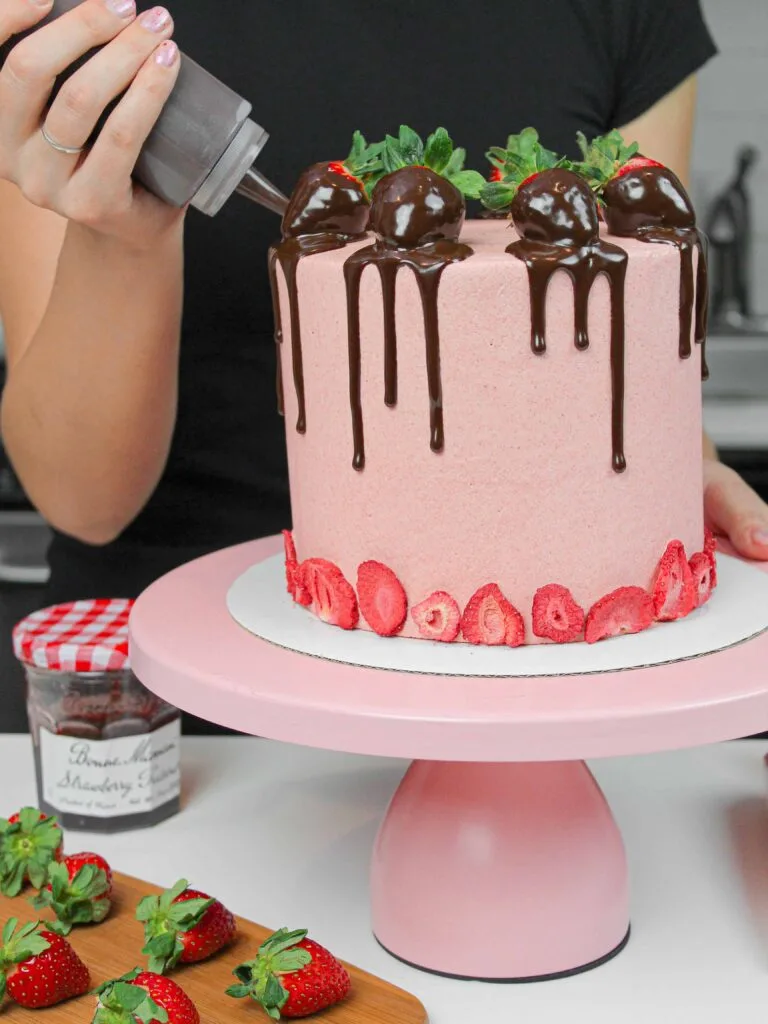 image of chocolate covered strawberry cake, with chocolate drips being added to the cake with a plastic squirt bottle