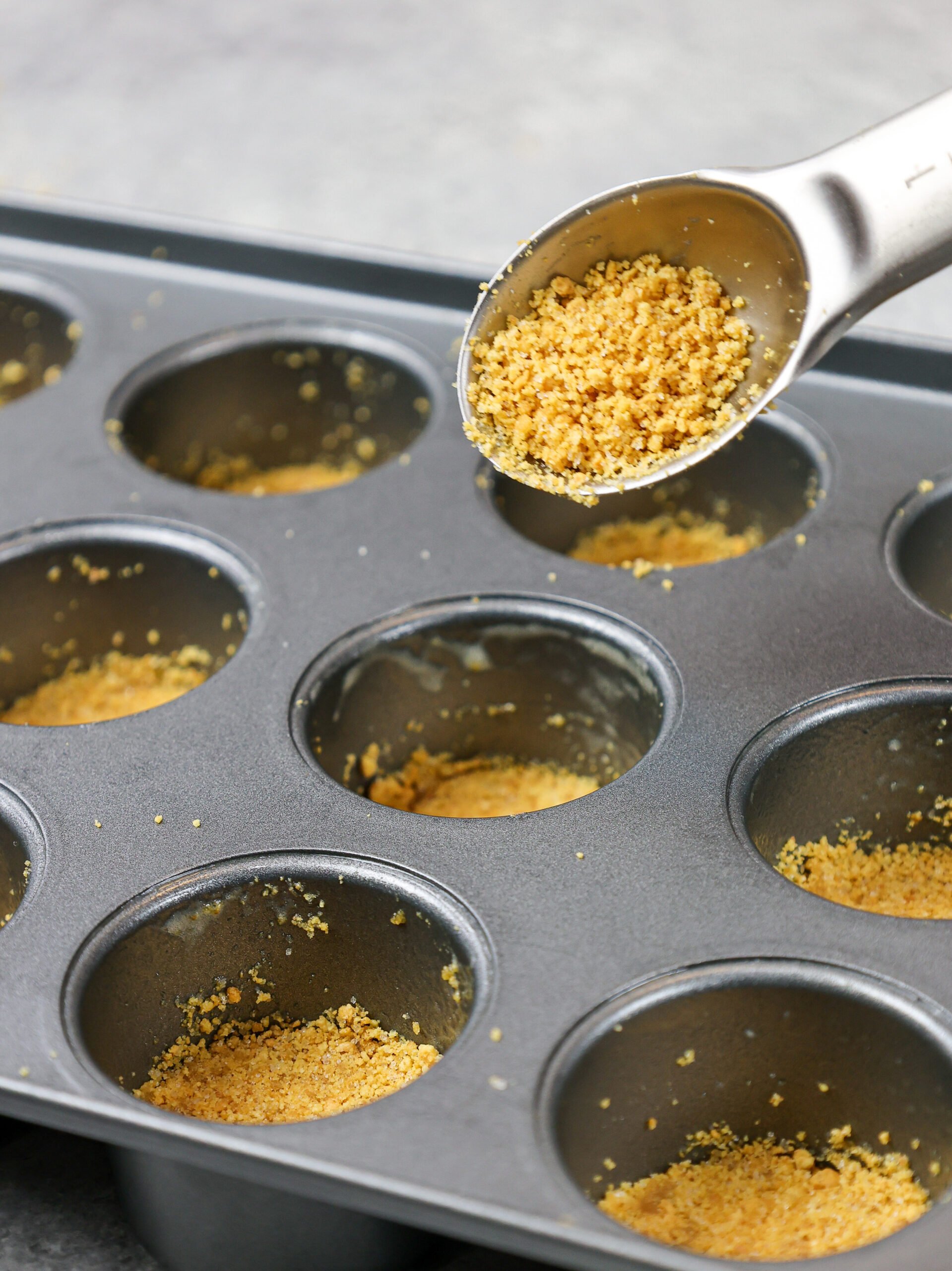 image of graham cracker crumbs being pressed into a mini cheesecake pan to make mini cheesecakes