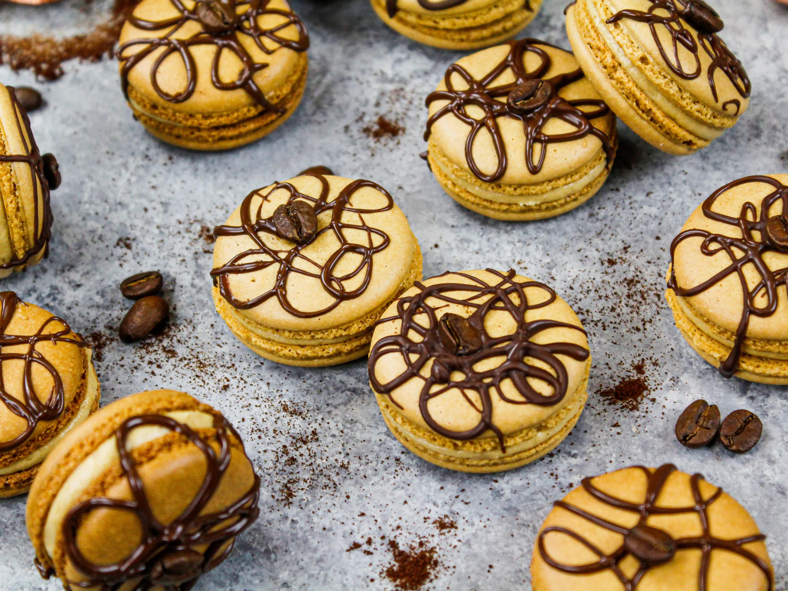 image of coffee macarons filled with coffee buttercream and decorated with a drizzle of dark chocolate and a coffee bean