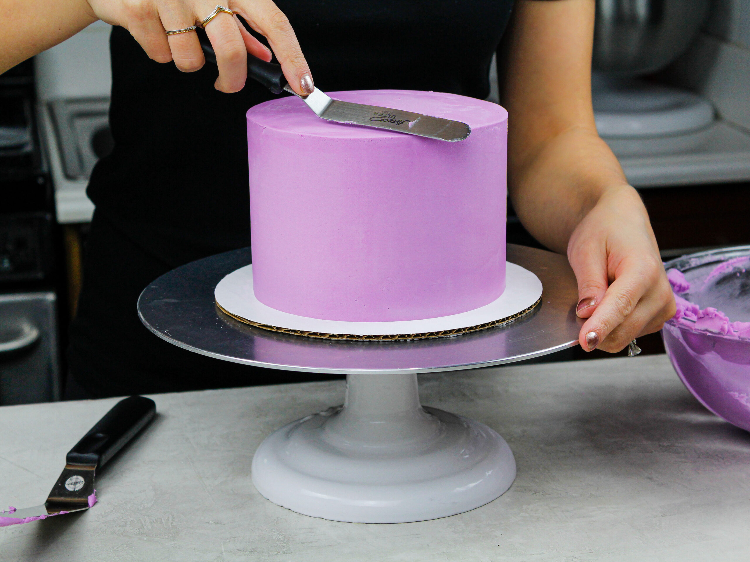 image of a purple cake being frosted with buttercream to have super smooth sides and sharp edges