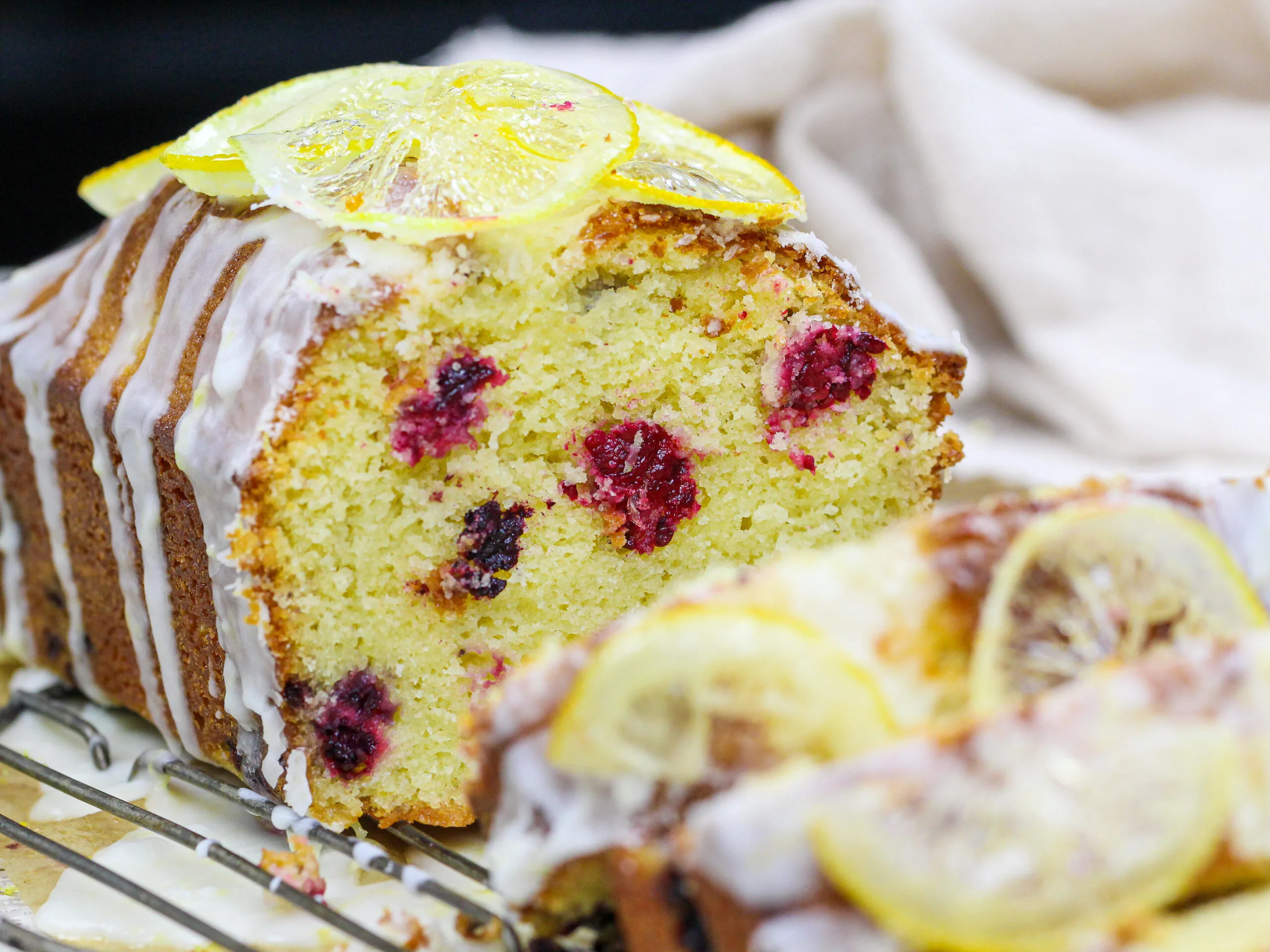 image of a sliced blackberry lemon bread drizzled with lemon glaze and topped with candied lemons