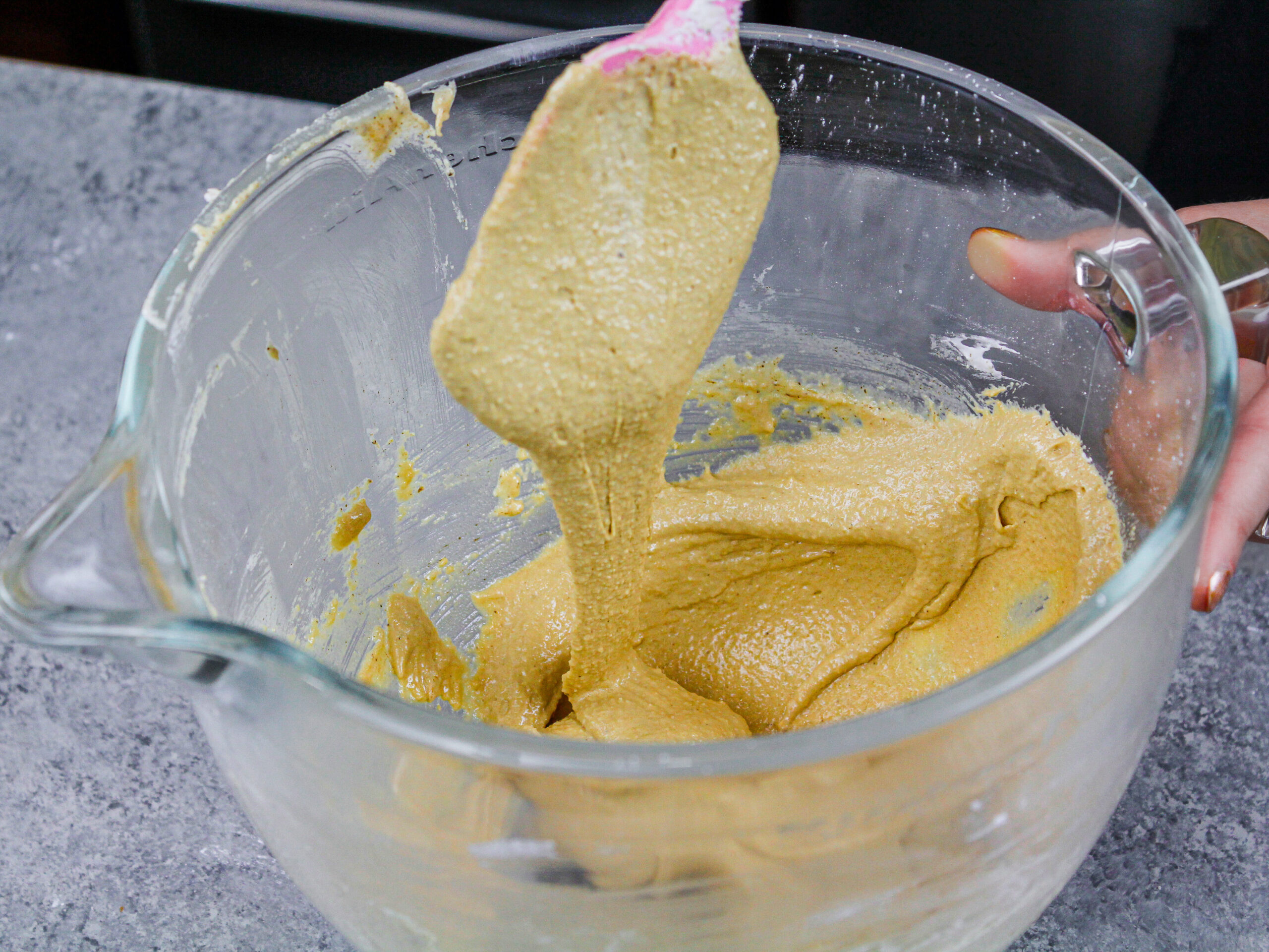 image of coffee macaron batter flowing off a spatula when lifted to show that is the perfect consistency and is ready to be piped