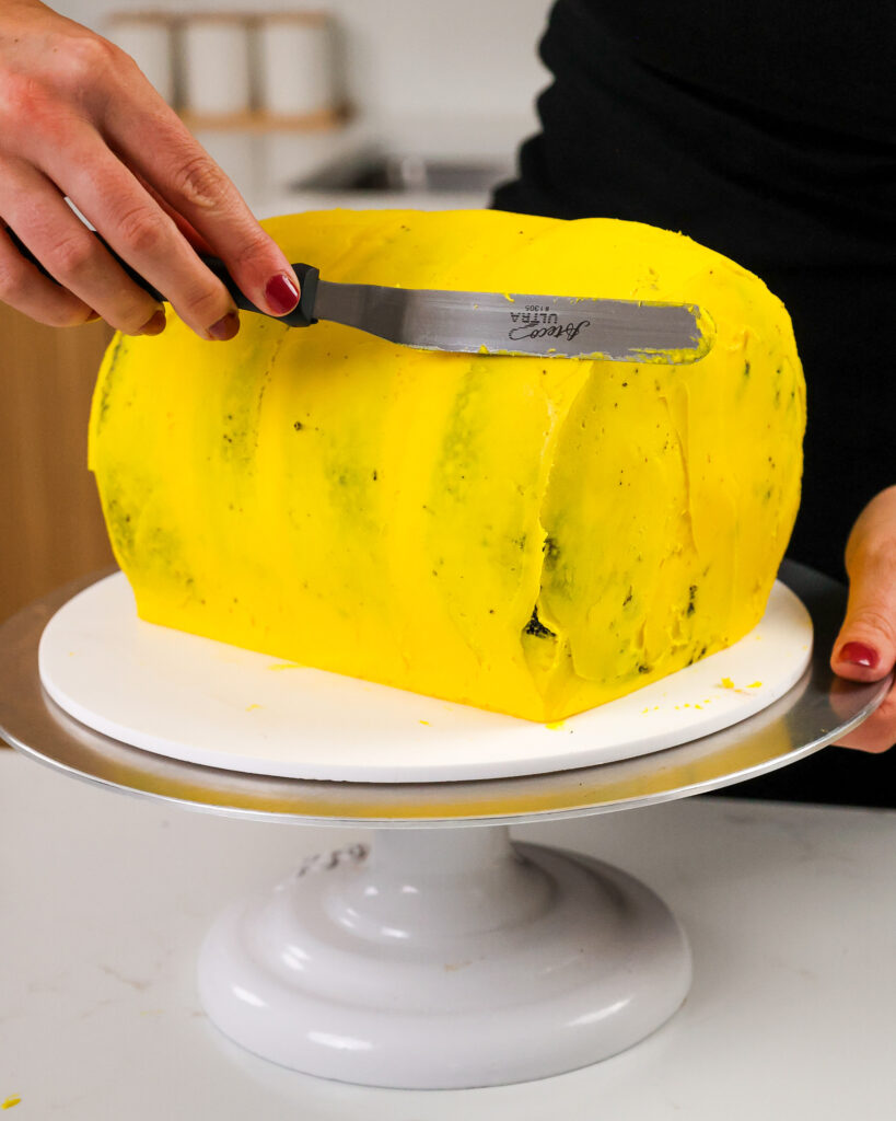 image of a chocolate cake being crumb coated with yellow buttercream frosting
