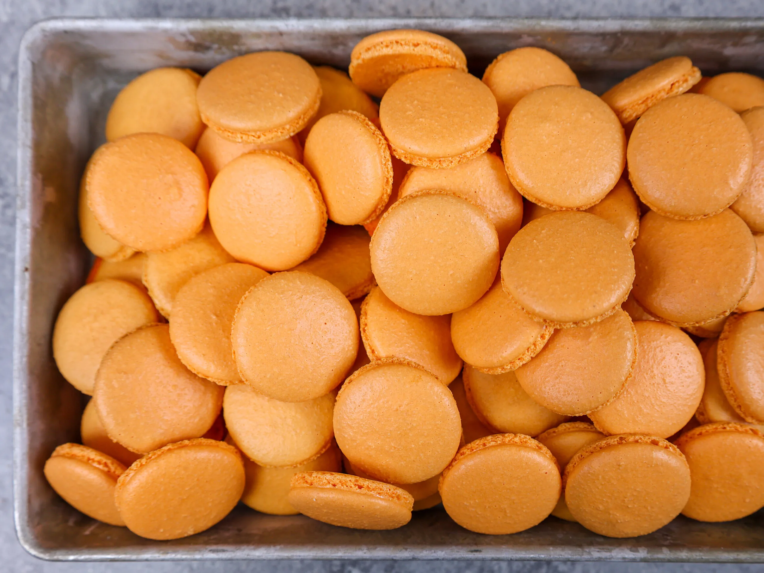 image of a tray of orange macaron shells that have been baked and cooled and are ready to be filled