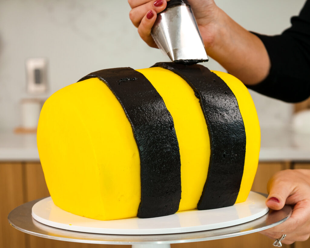 image of black frosting being piped onto a yellow cake to make a bumblebee birthday cake