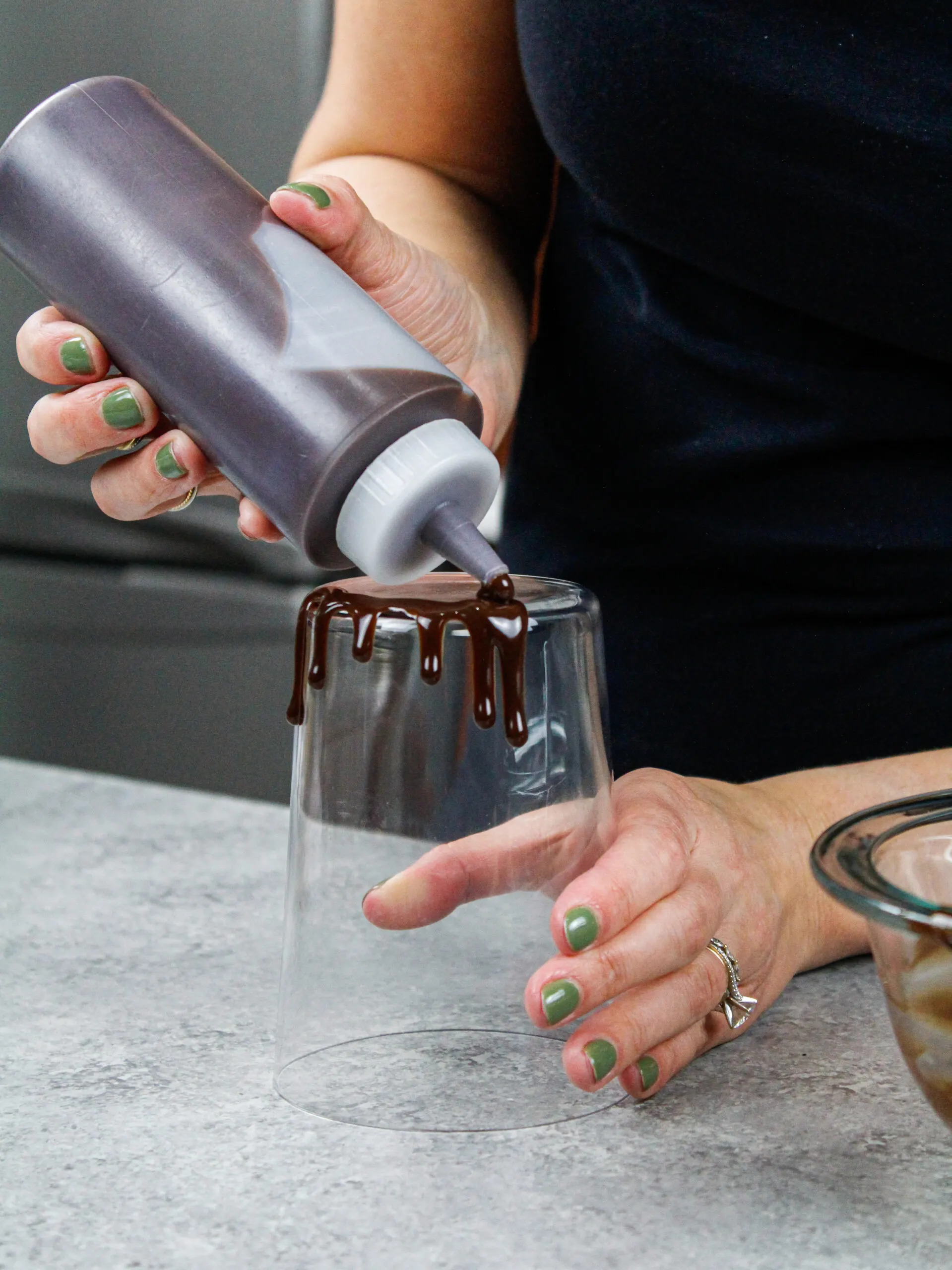 image of chocolate ganache drips being added around a tall glass to test its consistency and practice adding drips to a cake