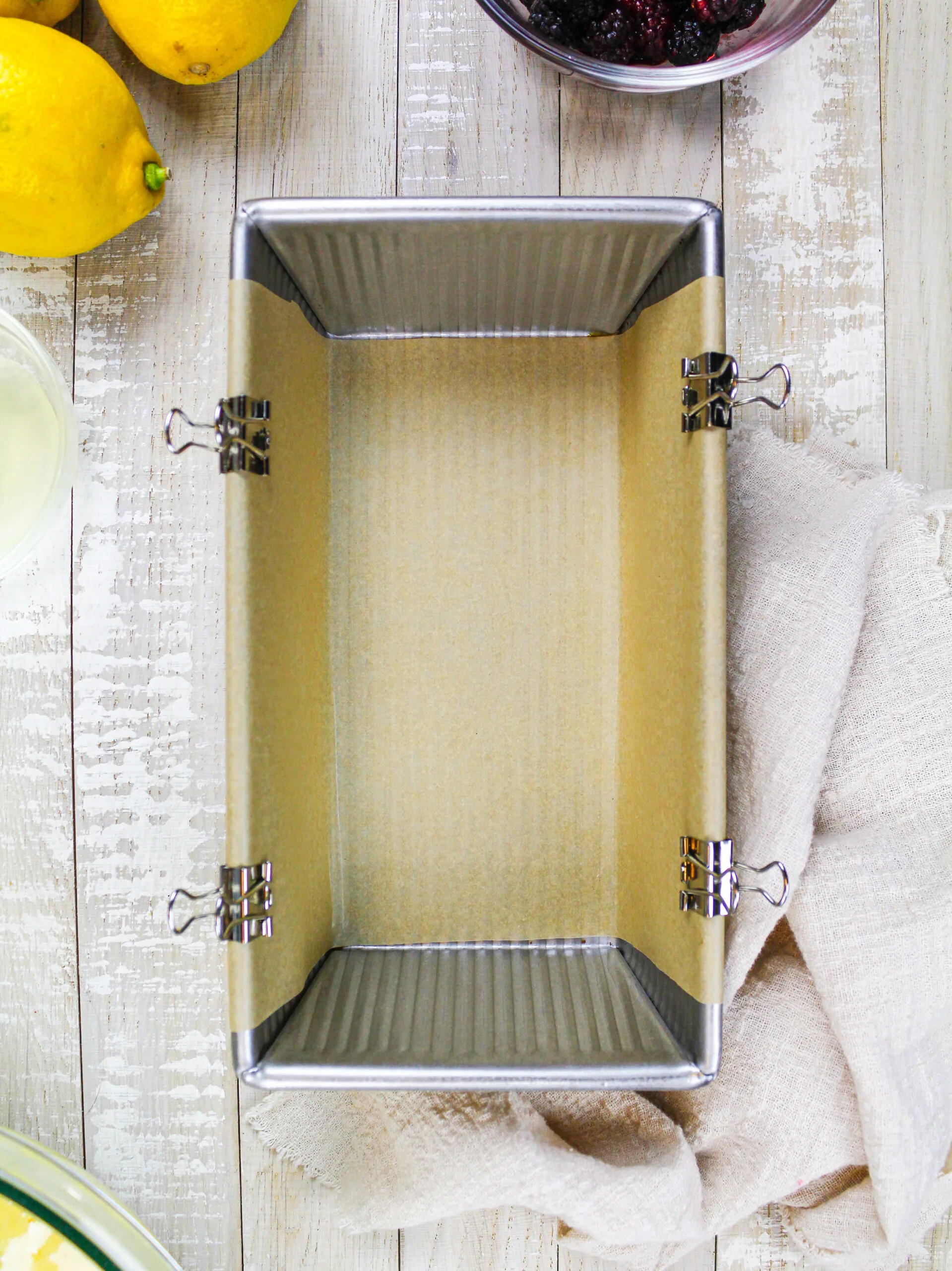 image of a loaf pan greased with non-stick spray and lined with a sling of parchment paper that's secured with metal binder clips