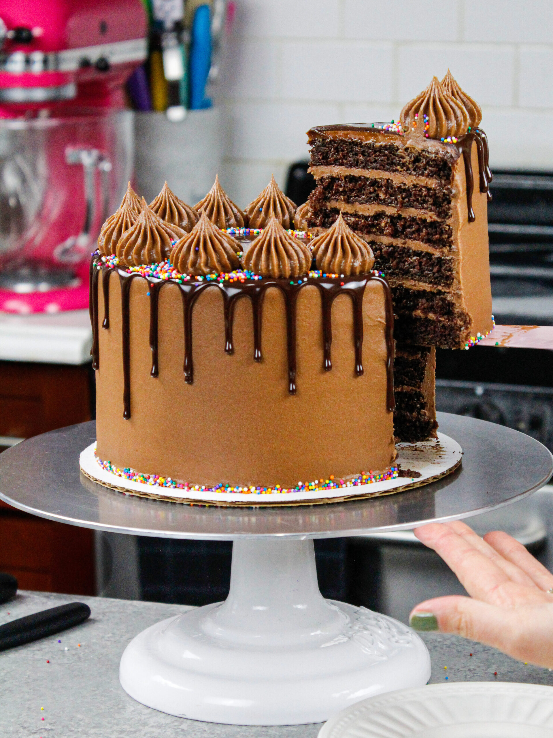 image of a chocolate drip cake that's been cut into and is having a slice pulled out to show it's six layers
