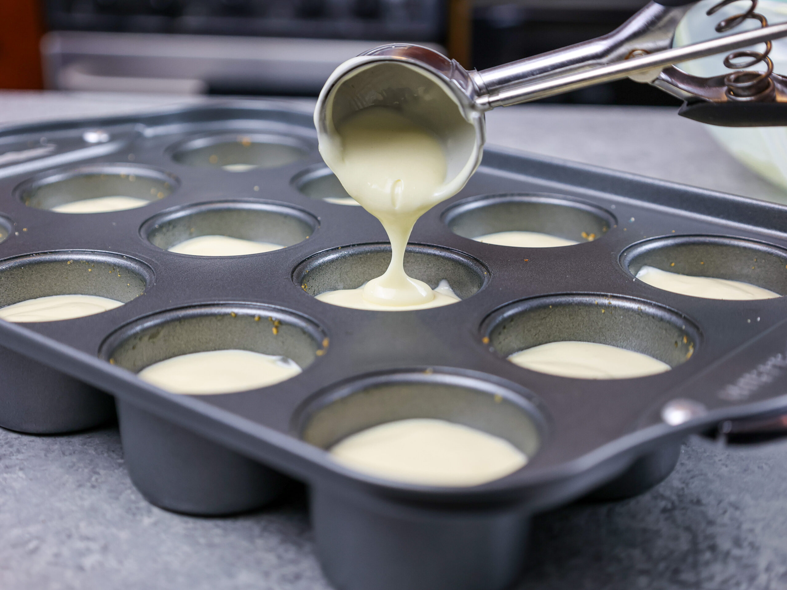 image of cheesecake batter being scooping into a pan to make mini strawberry cheesecakes