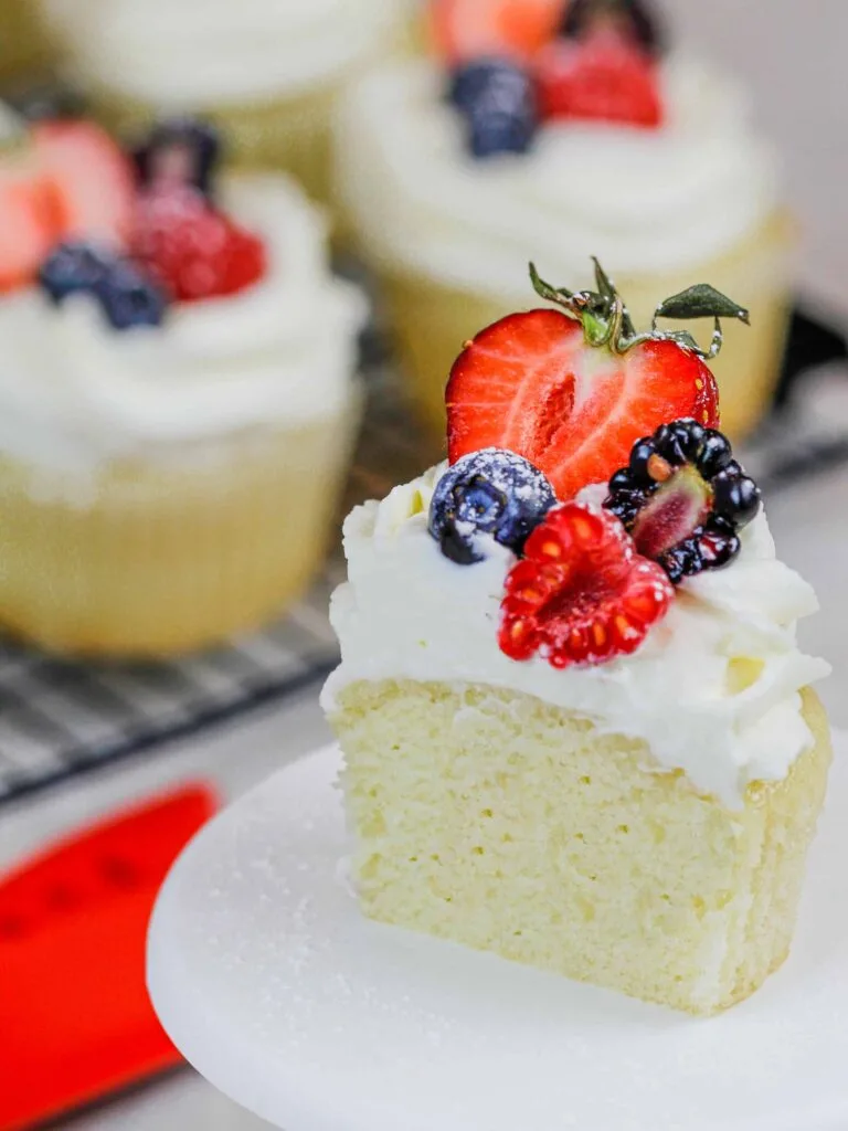 image of a cupcake that's been cut into and topped with whipped cream frosting and fresh fruit