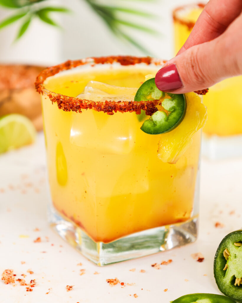 image of a garnish being added to a pineapple jalapeño margarita rimmed with tajin