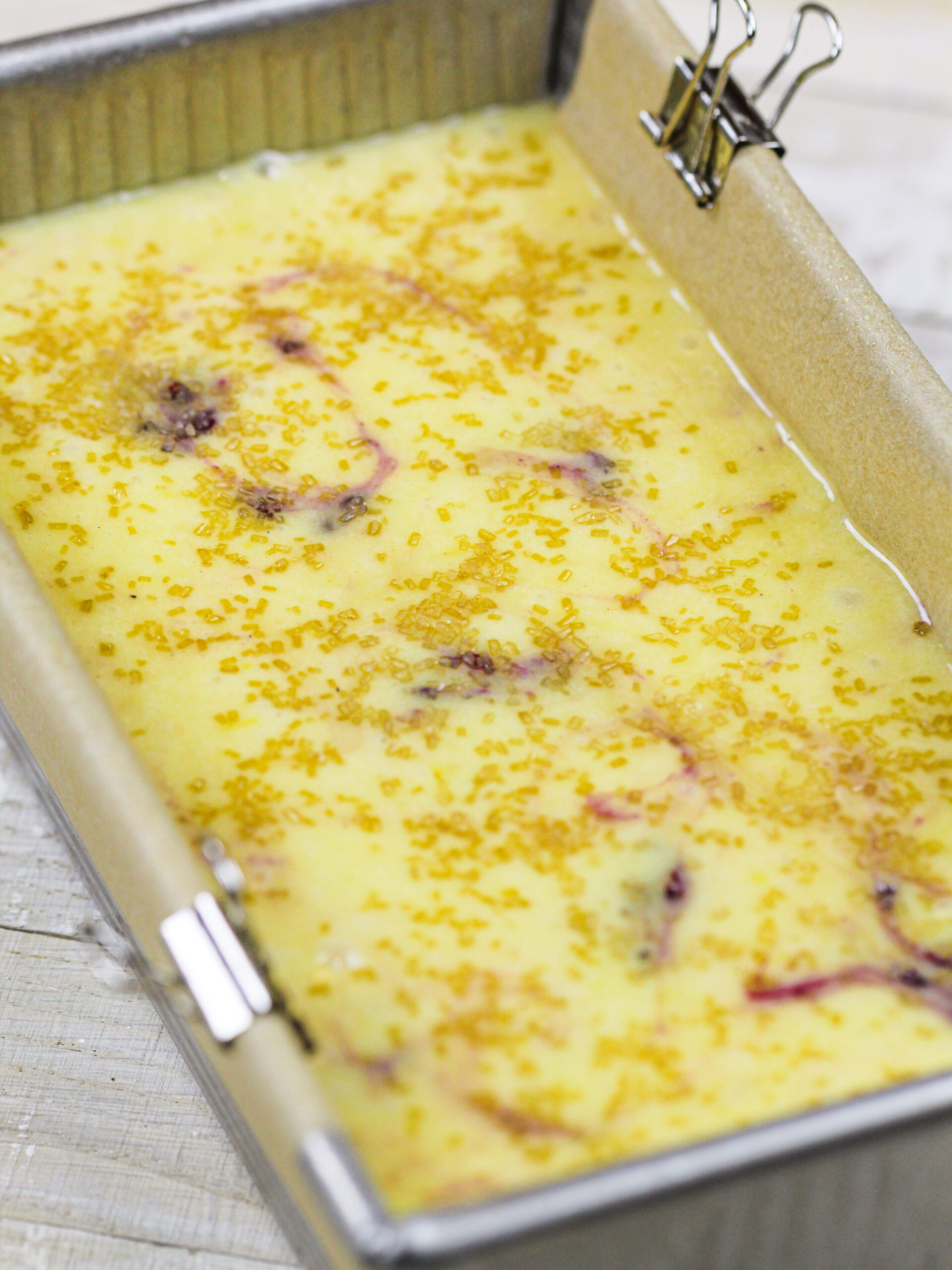 image of blackberry lemon bread batter in a loaf pan ready to be baked and topped with a sprinkle of turbinado sugar for a bit of extra texture