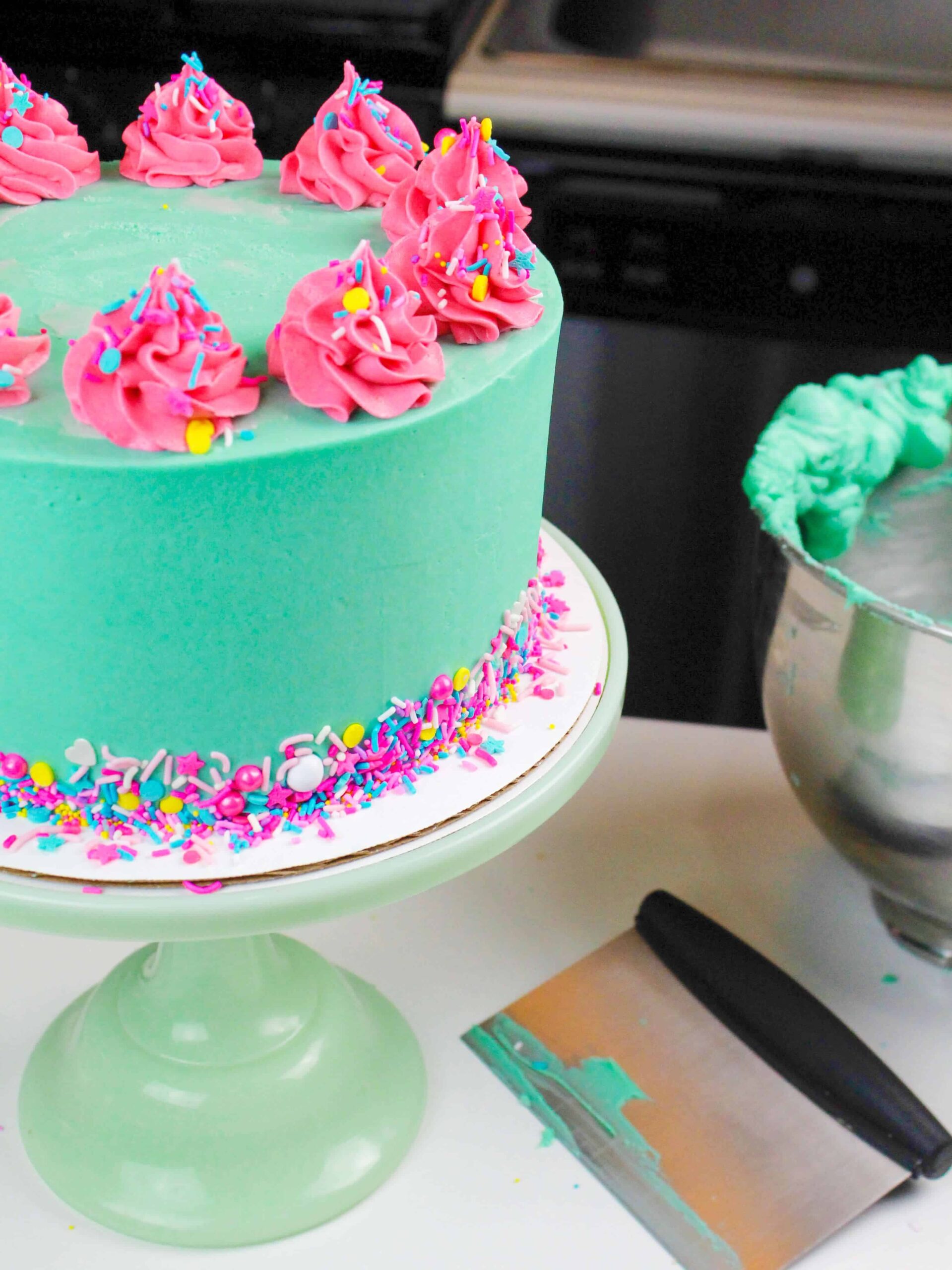 photo of frosted funfetti cake, decorated with turquoise teal frosting and pink frosting swirls 