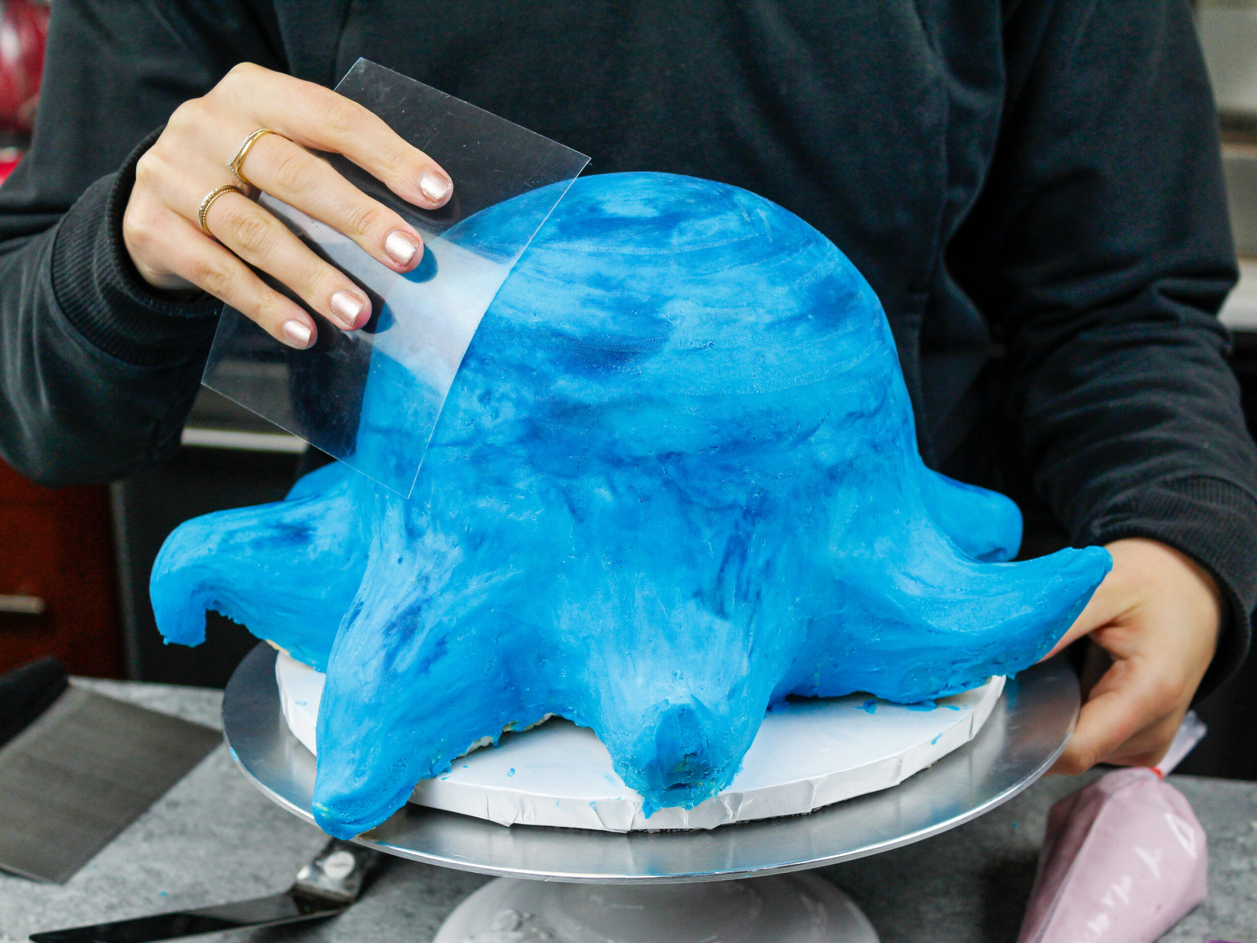 image of an octopus cake being frosted and smoothed using an acetate sheet