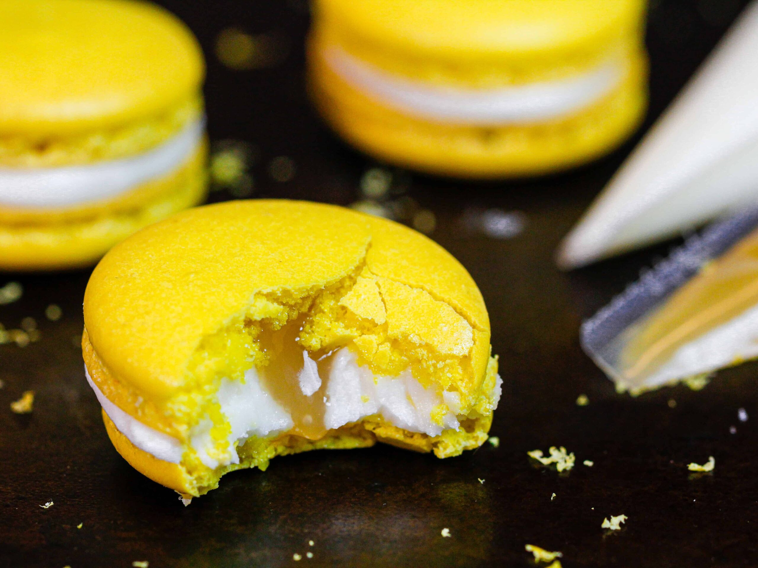 image of a lemon macaron that's been bitten into to show its lemon curd filling and fresh lemon buttercream