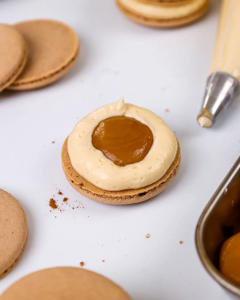 image of a salted caramel macaron that's being filled with thick caramel and caramel frosting