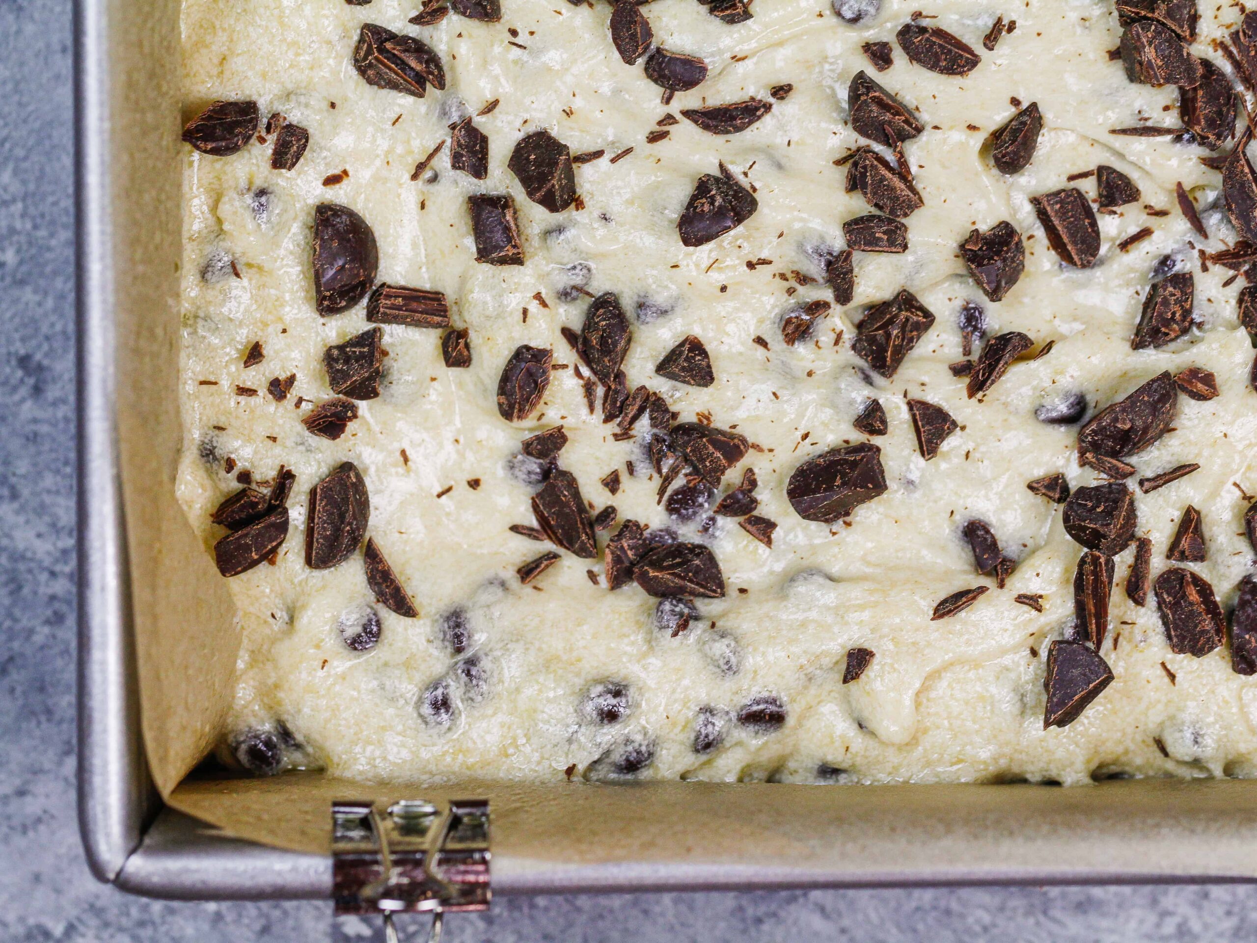 image of chocolate chip banana bar batter in a lined baking pan, ready to be baked in the oven