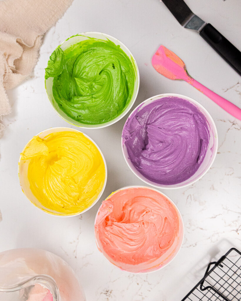 image of four bowls of frosting that have been colored green, purple, pink and yellow
