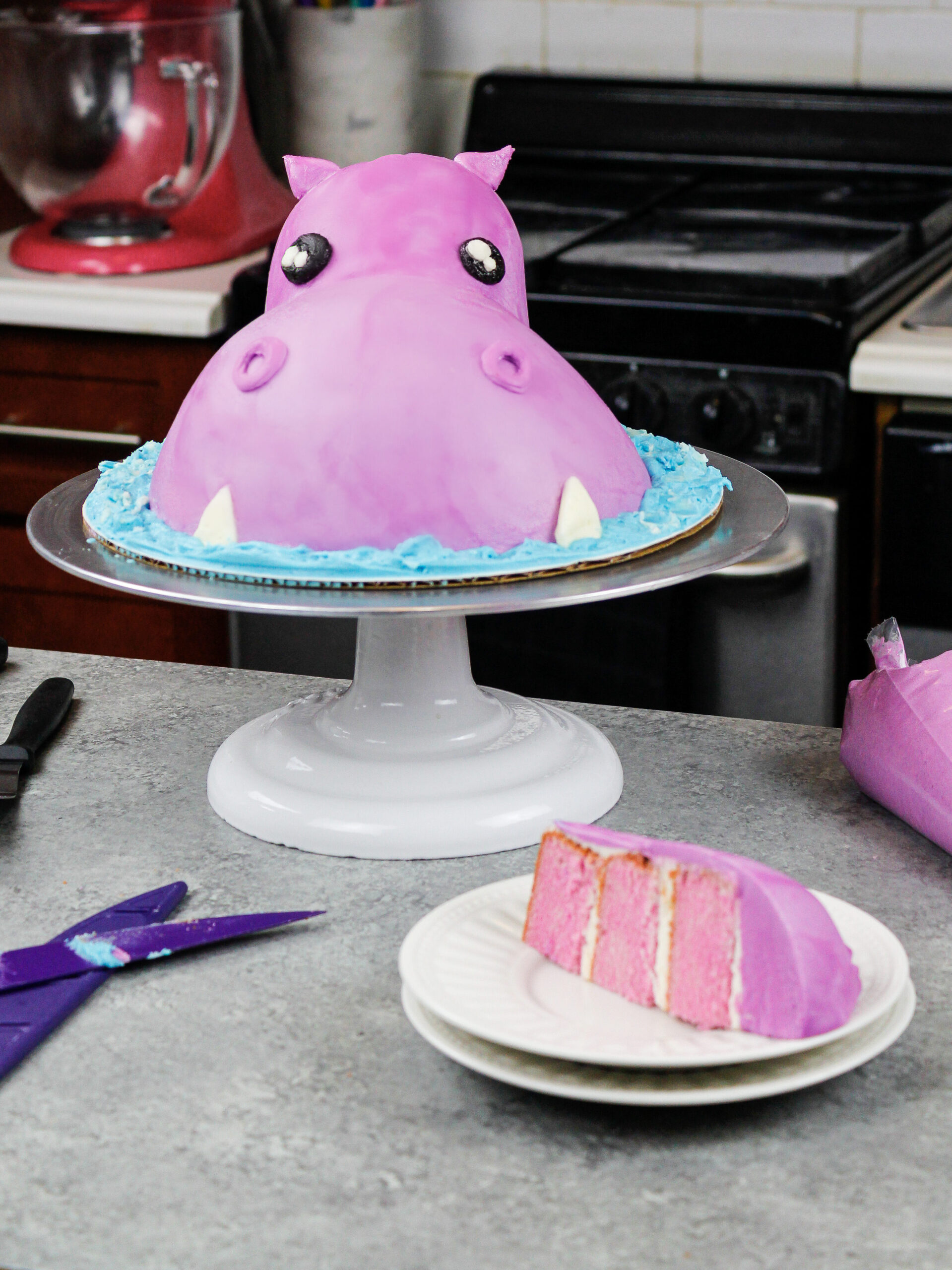 image of an easy buttercream hippo cake made for a child's birthday party with a slice cut out to show its matching purple cake layers