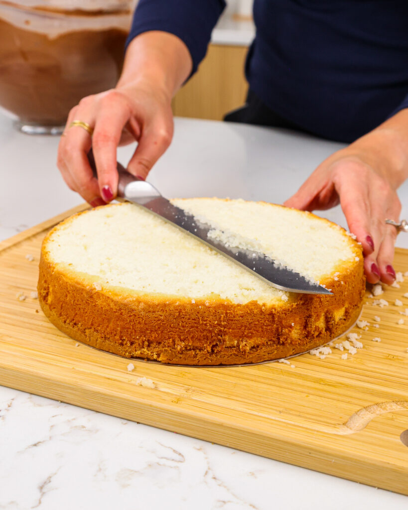 image of a shortbread crusted vanilla cake layer being leveled with a serrated knife