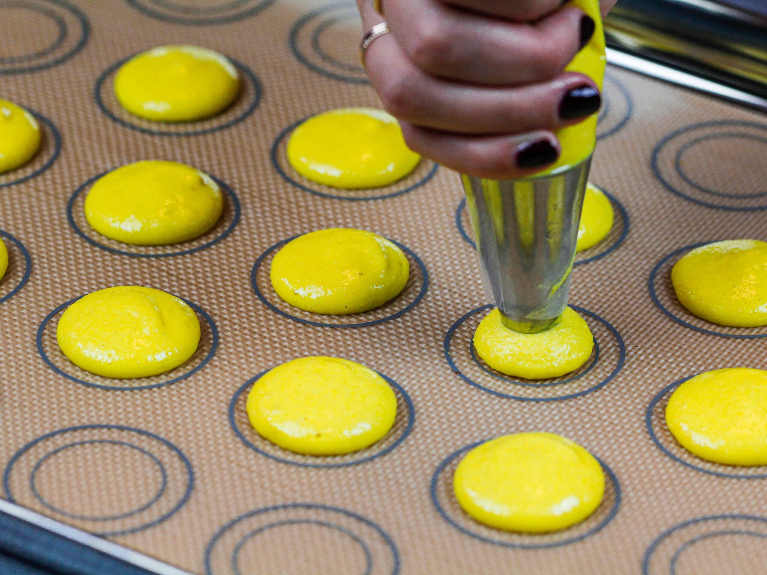 image of yellow macaron shells being piped onto a silpat mat