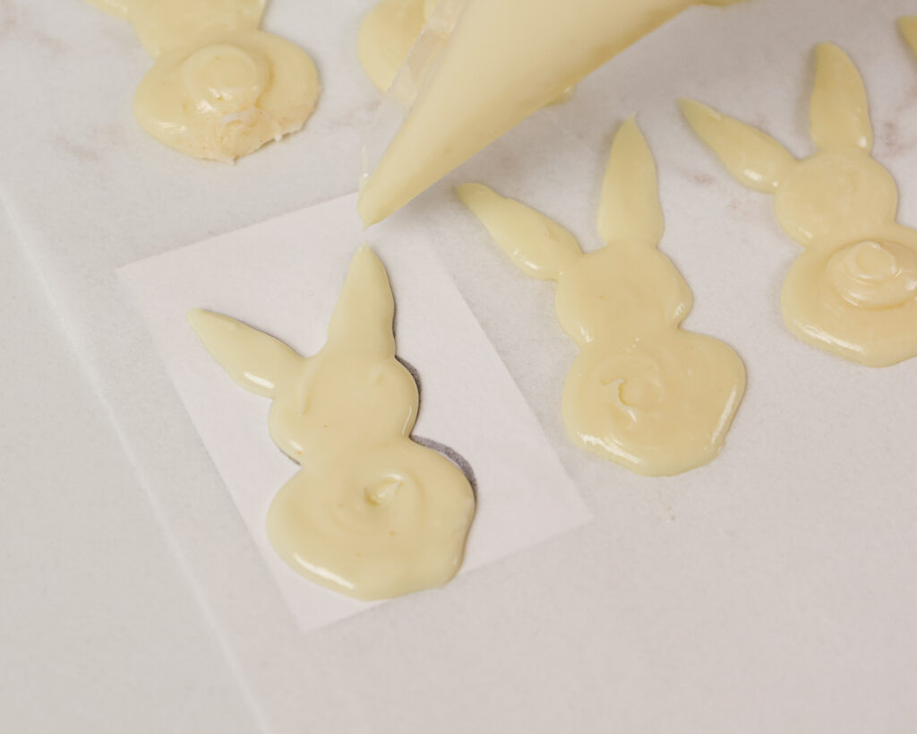 image of white chocolate bunnies being piped onto a piece of a parchment paper