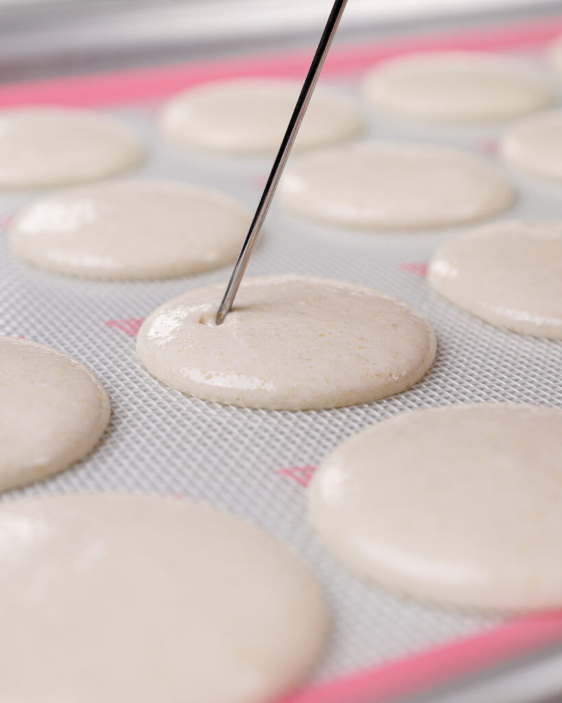 image of white macaron shells that have been piped and banged on the counter, and that are having any small bubbles that surfaced be popped with a scribe